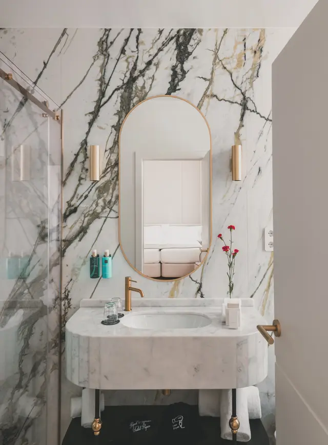 Baño de mármol con lavabo, espejo ovalado y grifería dorada en una habitación interior de La Fonda de los Príncipes