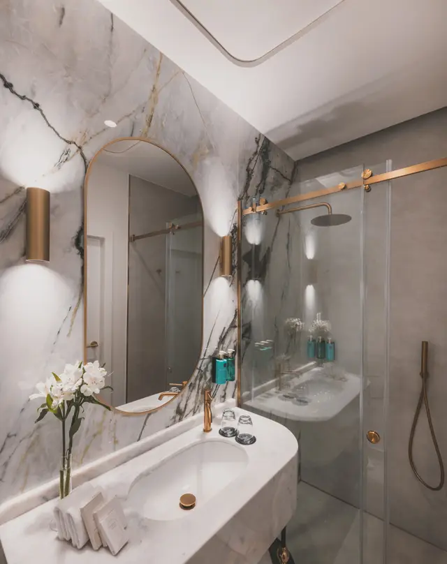 Baño de mármol con lavabo, ducha de mampara y espejo ovalado en una habitación de La Fonda de los Príncipes