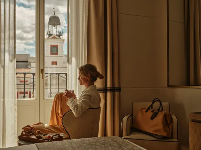 Woman in a bathrobe having coffee by the balcony, with the Real Casa de Correos clock behind