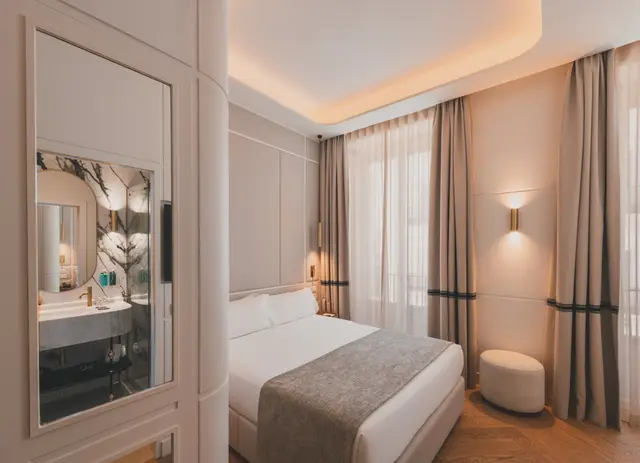 Espejo de armario que refleja el baño, junto a la cama y el puf de la Deluxe Exterior