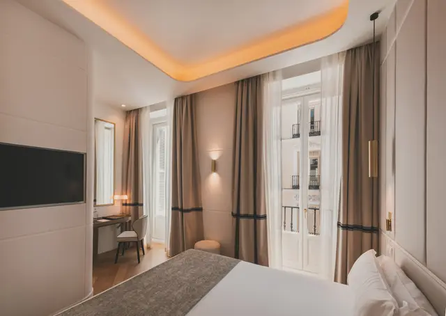Cama, escritorio y Smart TV junto a la puerta del balcón en la Deluxe Exterior, con iluminación indirecta