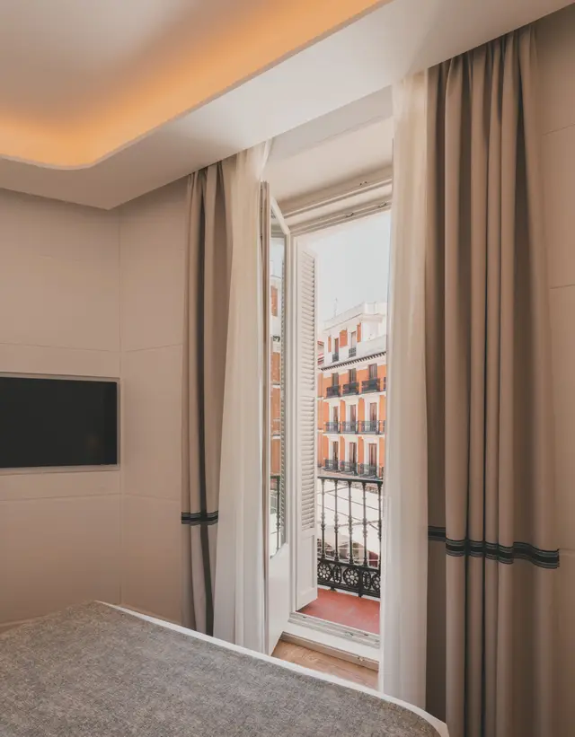 Cama y Smart TV junto a la puerta del balcón con vistas a la fachada de enfrente en la Deluxe Exterior