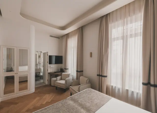 Cama con armario de espejos, escritorio y ventanal con cortinas en la habitación Deluxe Interior