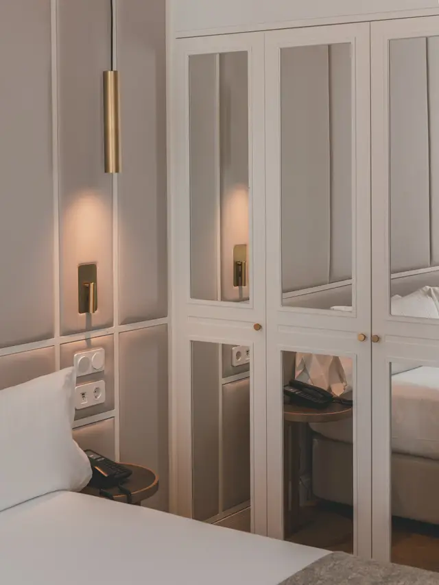 Cama junto al armario de espejos con lámpara colgante dorada en la habitación Deluxe Interior