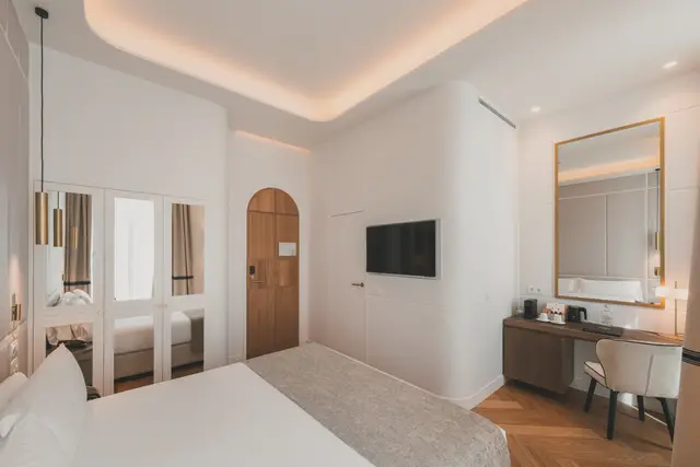Habitación Deluxe Lateral Sol con cama, armario de espejos, puerta de madera en arco y escritorio