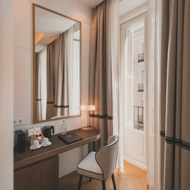 Escritorio con espejo de marco dorado y puerta del balcón abierta en la habitación Deluxe Lateral Sol