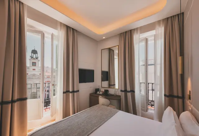 Habitación Deluxe Vista Sol con cama y ventanales abiertos al reloj de la Real Casa de Correos