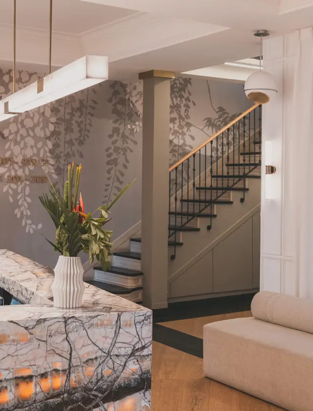 Escalera junto a la recepción, con papel pintado de mármol, sofá y una planta