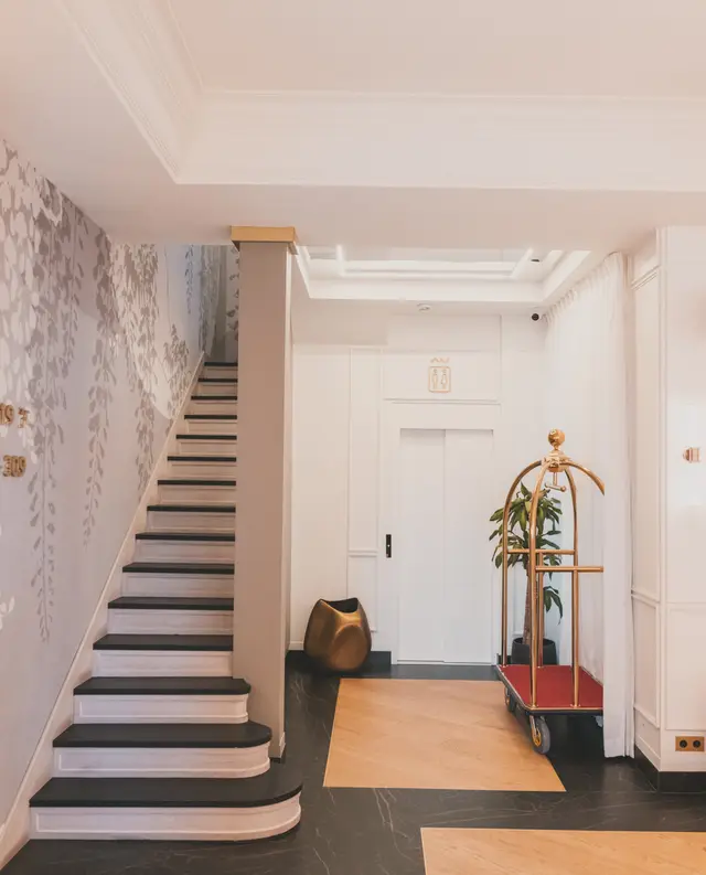 Lobby staircase with marble-pattern wallpaper and a gold luggage cart