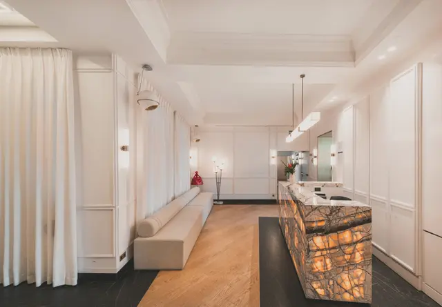 Recepción del hotel con mostrador de mármol, banco corrido y cortinas claras