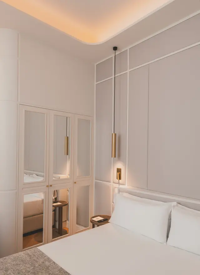 Cama junto al armario de espejos y una lámpara colgante dorada en el Estándar Interior