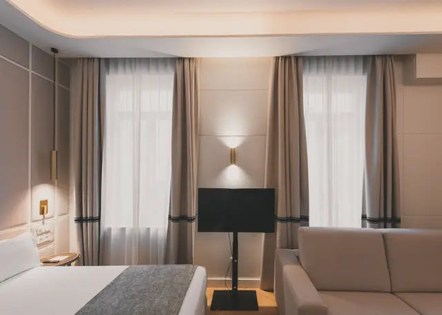Cama, Smart TV y sofá junto a las cortinas de la Junior Suite Interior Familiar