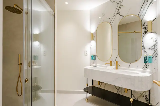 Bad mit Doppelwaschbecken aus Marmor, ovalen Goldspiegeln und Dusche im Premium Corner