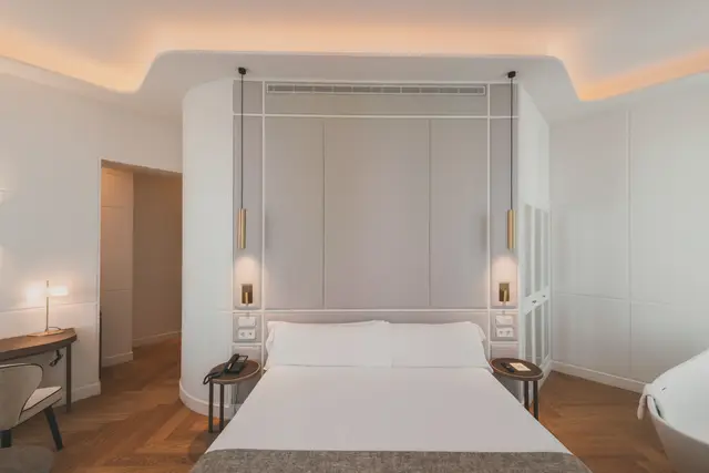 Cama con cabecero tapizado, lámparas colgantes doradas, escritorio y bañera exenta en la Premium Corner con bañera