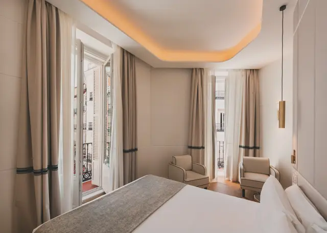 Cama frente a las puertas de los balcones con cortinas y butacas en la Premium Corner con ducha