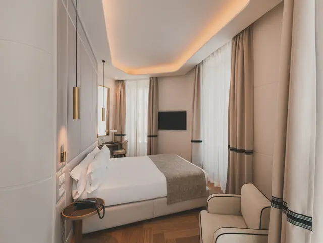 Habitación Premium Corner con ducha: cama, butaca y cortinas bajo una iluminación indirecta cálida